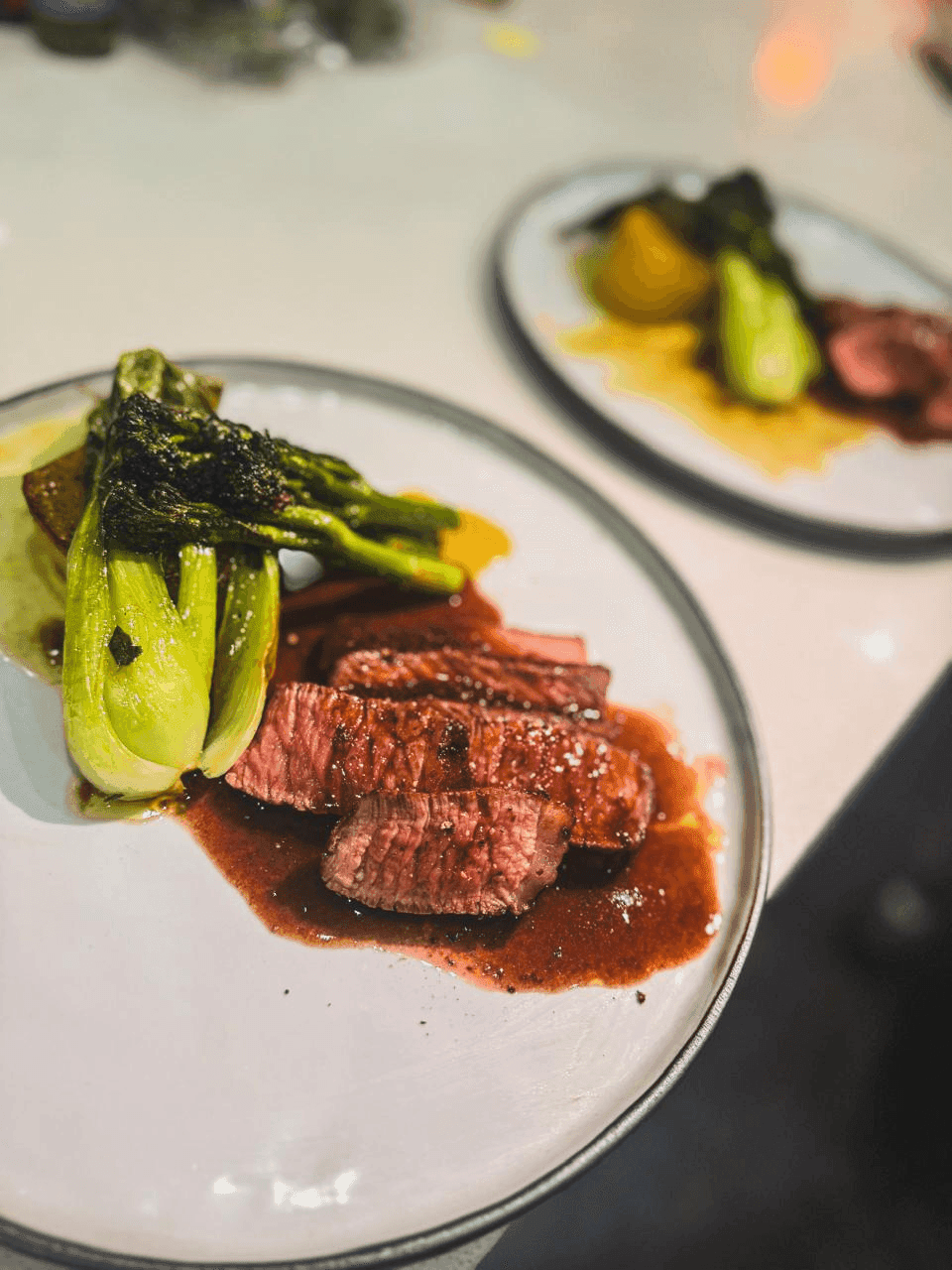 A reverse-seared rib eye course, plated with broccolini and a red wine jus.